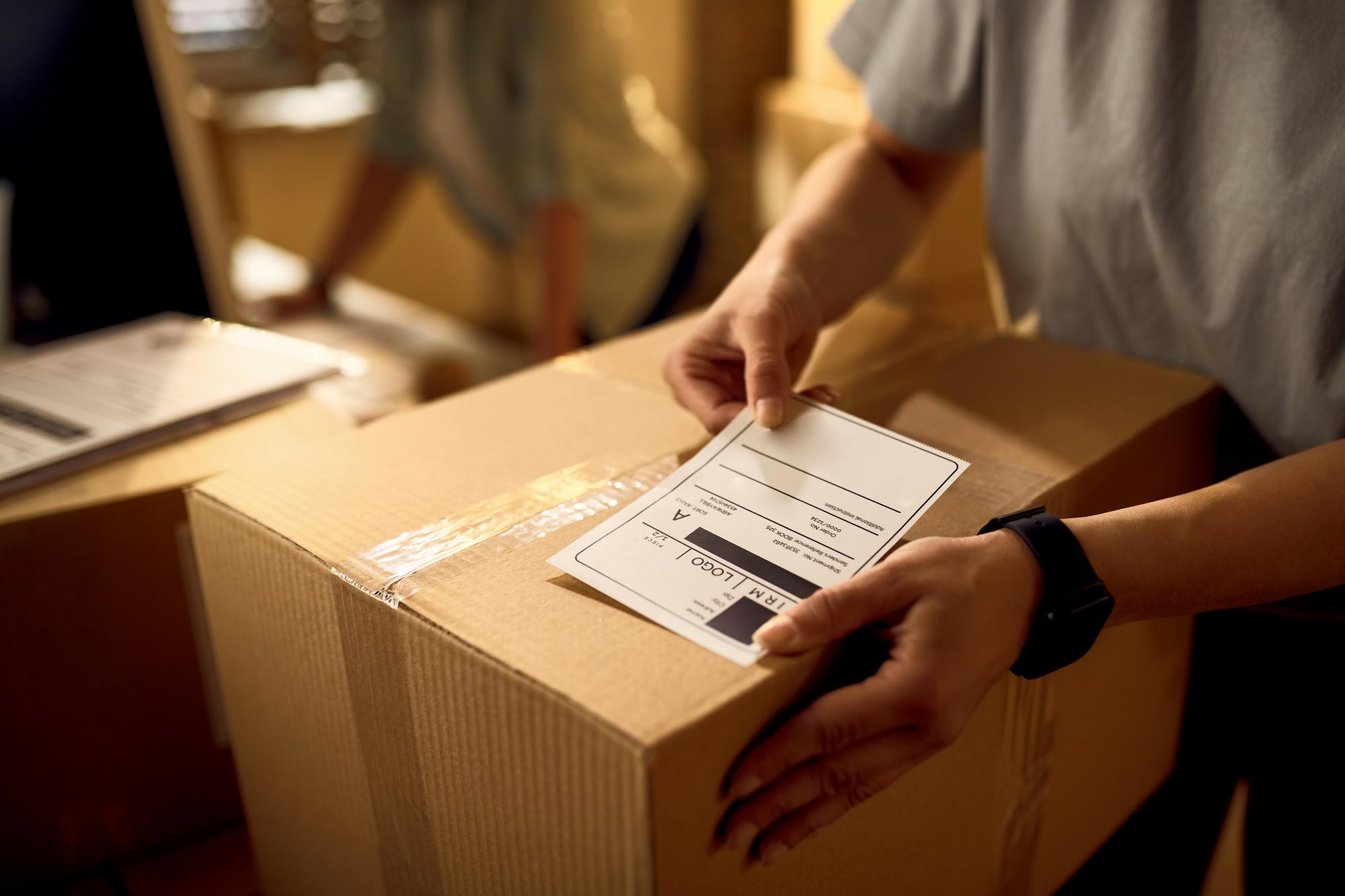 closeup-courier-attaching-address-label-package-while-working-office